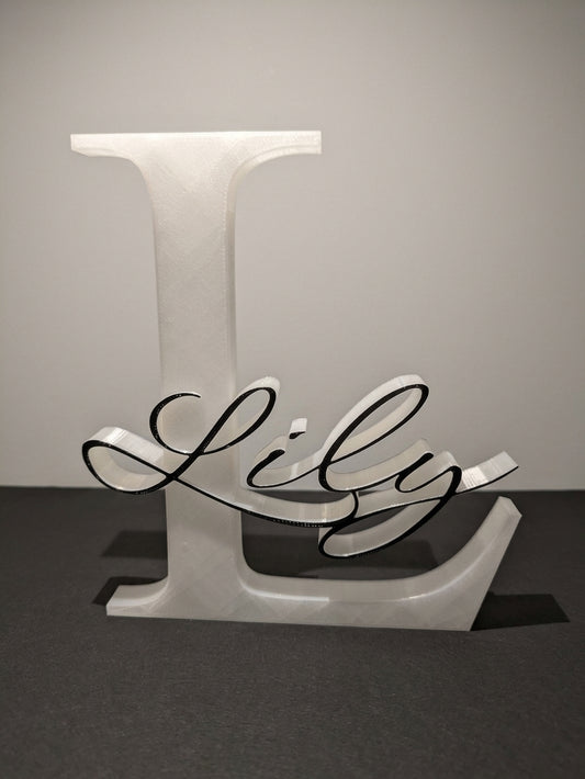 3D-printad namnskylt med stor vit bokstav L och namnet Lily i svart skrivstil